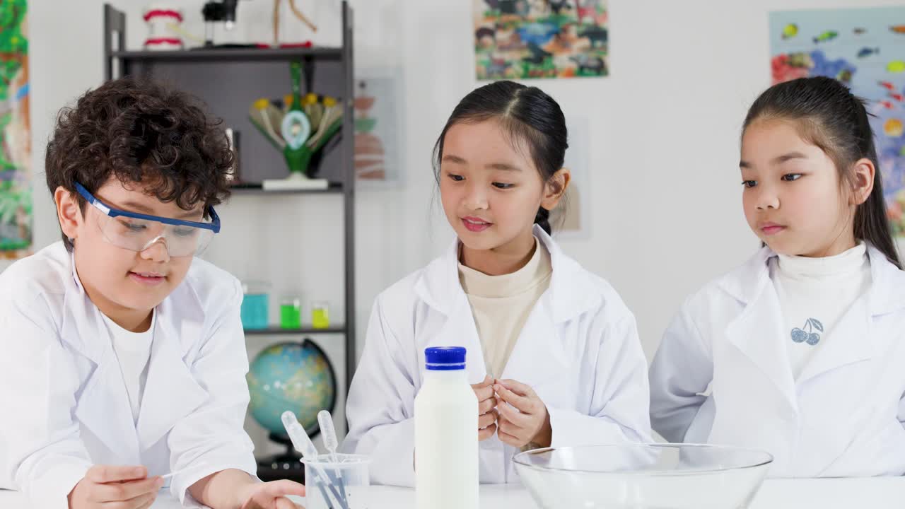 白衣と安全ゴーグルを着用した3人のタイの子供たちが、一緒に化学実験を行っています。