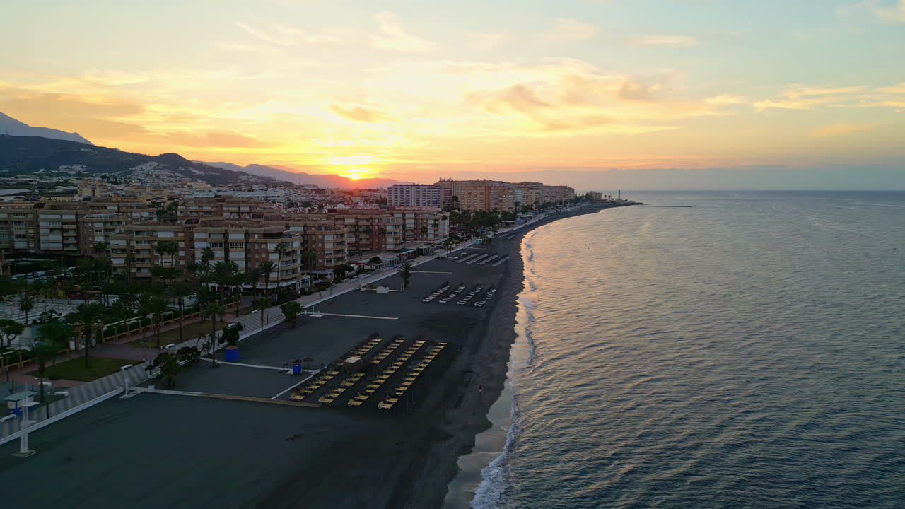 drone aéreo en movimiento hacia adelante filmado sobre la hermosa playa a lo largo de la ciudad costera de fuengirola en málaga, españa al amanecer