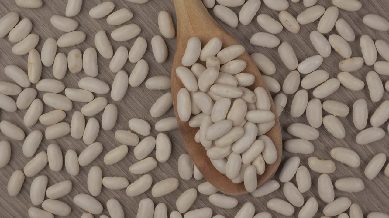 White dry beans legumes on wooden spoon rotating. Vegan vegetarian ingredient, Mediterranean diet
