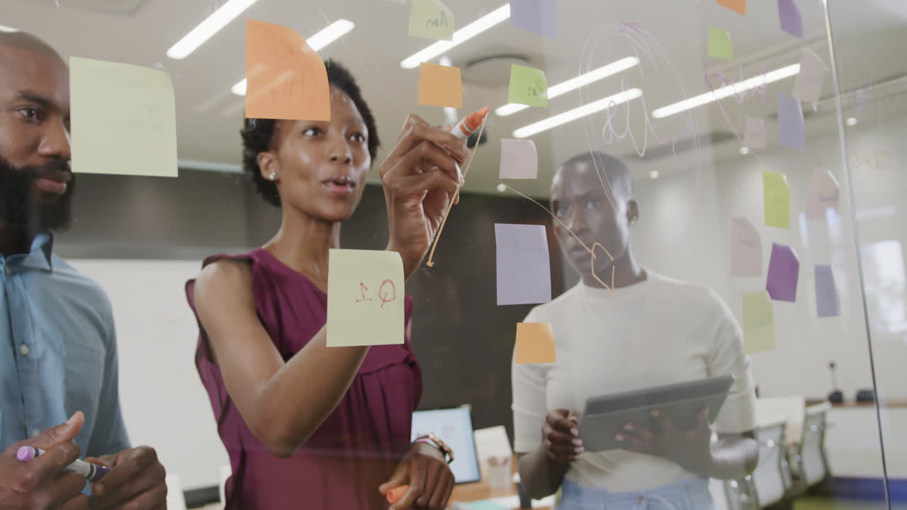 African american colleagues brainstorming, making notes on glass wall in office in slow motion