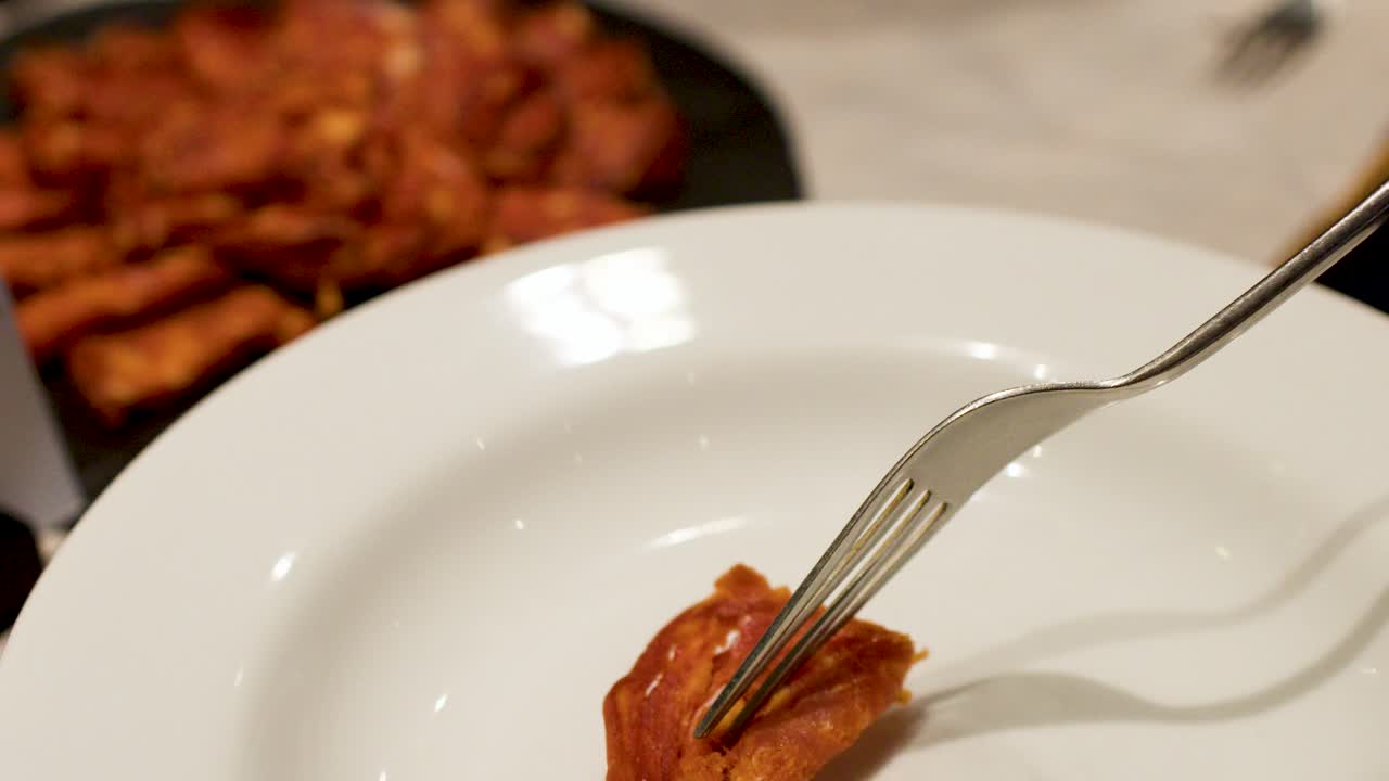 Detailní záběr ruky, která vidličkou nabírá chorizo z talíře
