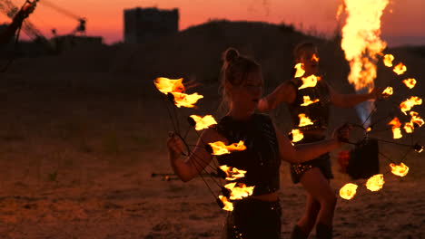 un hombre con un impermeable con dos lanzallamas deja salir una llama ardiente de pie al atardecer en la arena