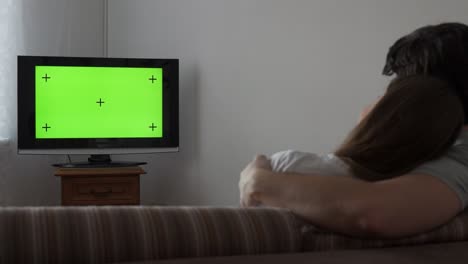 couple watches green mock-up screen tv while sitting on a couch in the living room