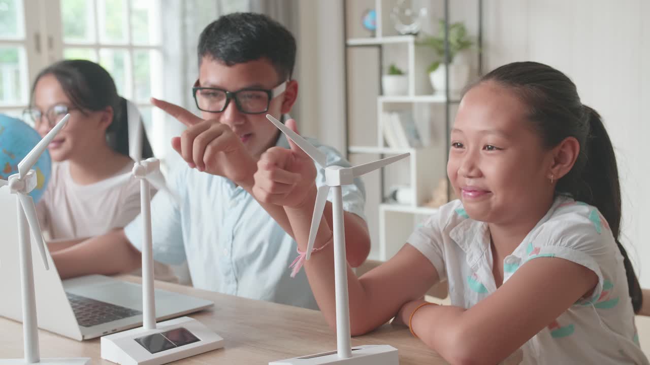 Asian Children Work As A Team Using Laptop Computers To Program Wind Turbines. Classroom With Kids Learning About Eco-Friendly Forms Of Renewable Energy