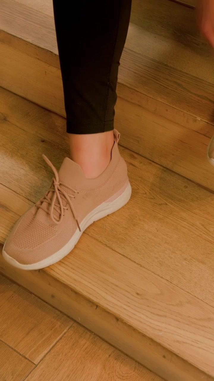 Vertical video: Pulling untied lace, person in leggings tucking into pink knit shoe on step to fit