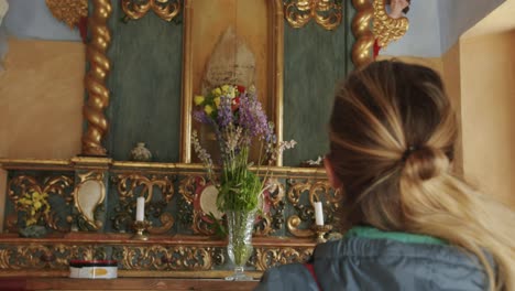 A-blond-young-girl-admiring-the-interior-of-a-small-church-called-Sant'Anna-in-the-mountains-of-Gressoney-La-Trinitè,-in-Italy,-near-Monte-Rosa