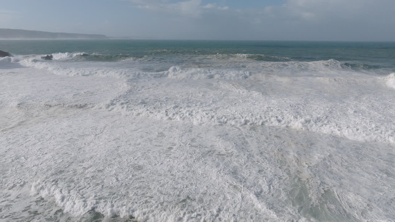 Aerial drone shot of big waves coming into shore on a day with giant waves in Nazaré, Portugal, Europe. View from beach. Tow-in surfing hotspot