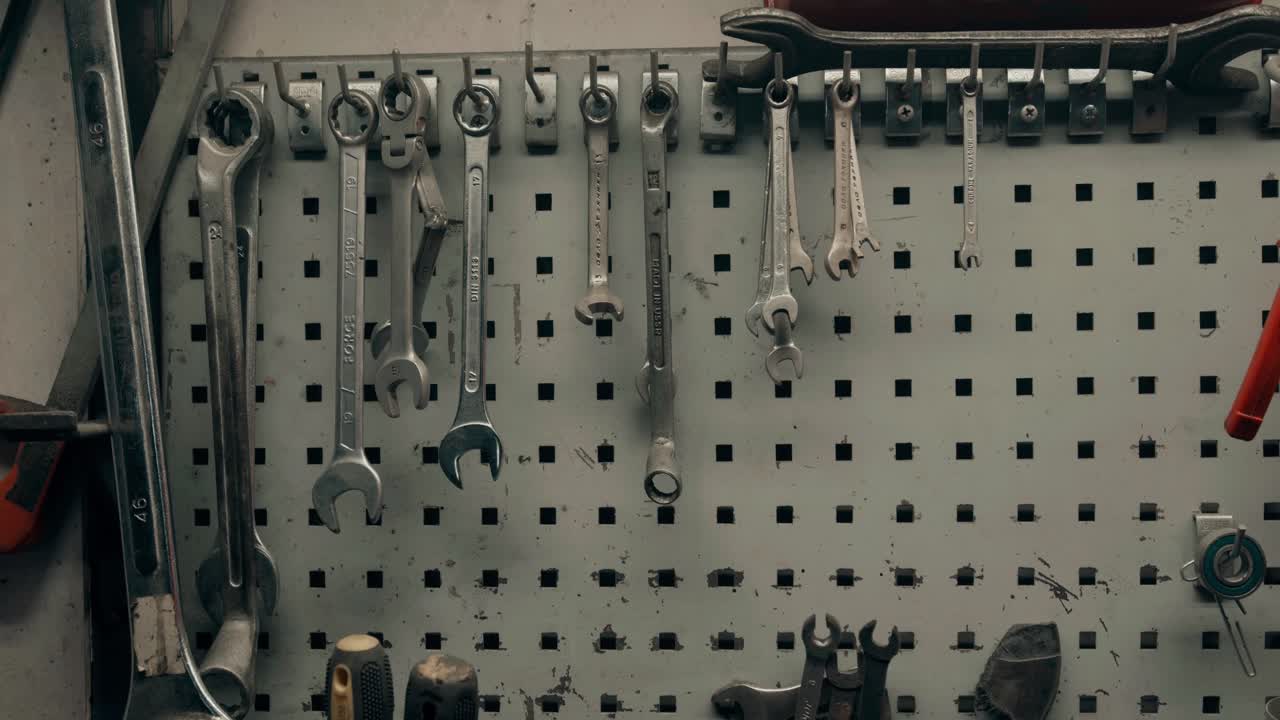 Someone taking a spanner from the tools hanging on the wall in a workshop