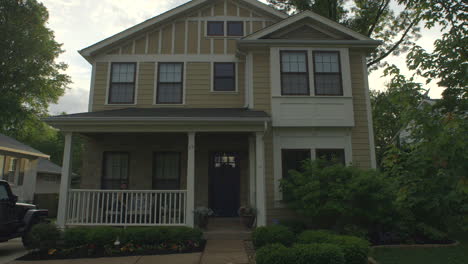 Front-view-of-suburban-house-in-the-summer-as-a-woman-sits-down-on-a-couch-on-the-front-porch