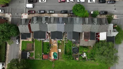 row of homes with narrow yard in american town. parking and driving cars in street. sunny spring day in united states. aerial top down rising shot.