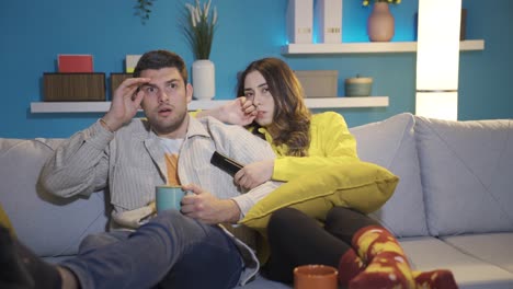 happy couple sitting on sofa at home at night watching horror and thriller movies on tv.