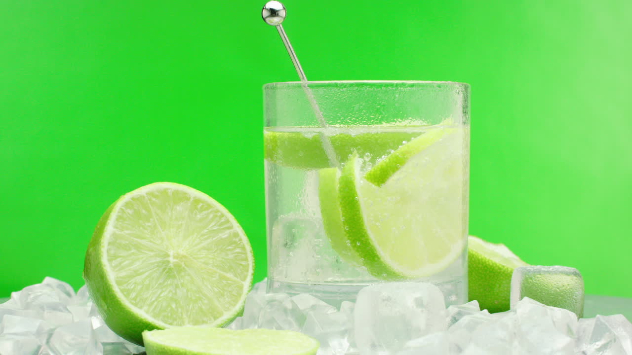 상쾌한 진 토닉, 녹색 레몬과 얼음 블록이 포함된 알코올성 여름 음료, 녹색 배경에 격리된 턴테이블에서 회전하는 슬로우 모션 제품 비디오