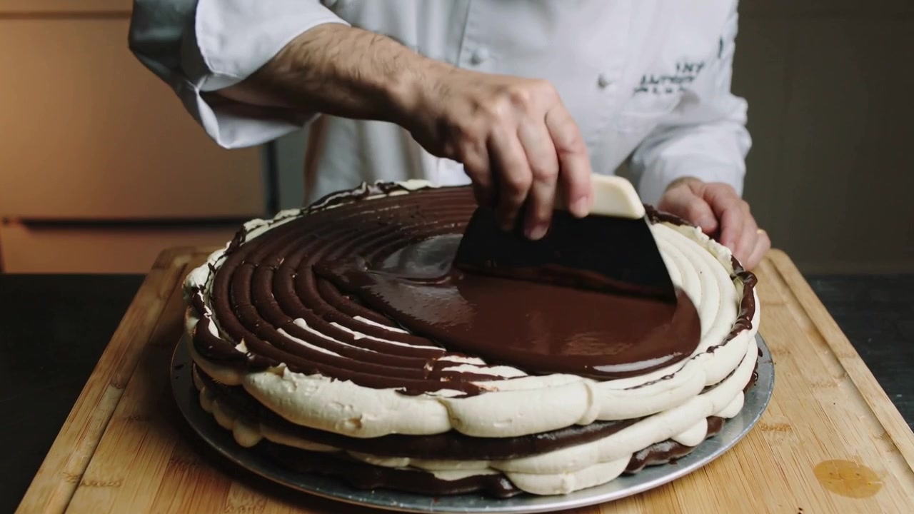 Spatola, chef in giacca bianca che spalma la ganache su una torta in cucina creando una finitura lucida