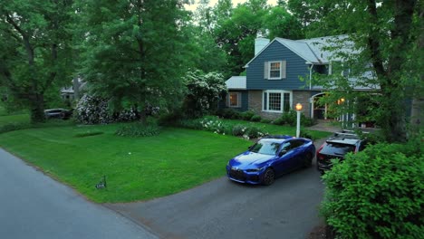parking cars in front of single family house in idyllic neighborhood of american town. quiet real estate in suburb district of usa in dusk. aerial approaching shot.