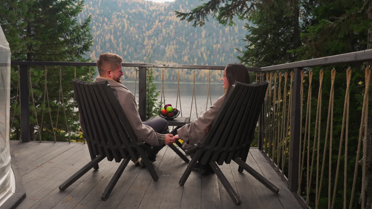 una pareja relajándose en un balcón de madera con vistas a un lago de montaña