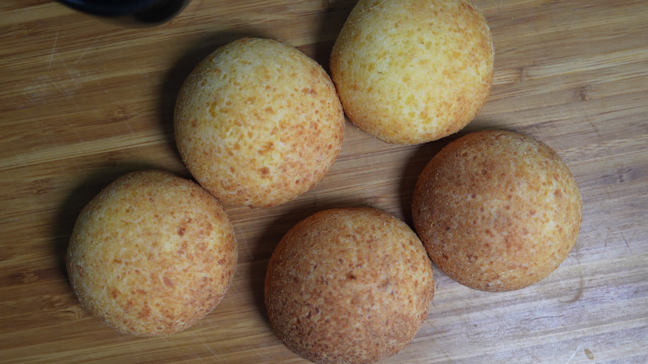 A close-up of five golden-brown almohabanas beside a cup of coffee on a rustic wooden table. Warm lighting enhances the cozy, inviting atmosphere, evoking Colombian culinary charm