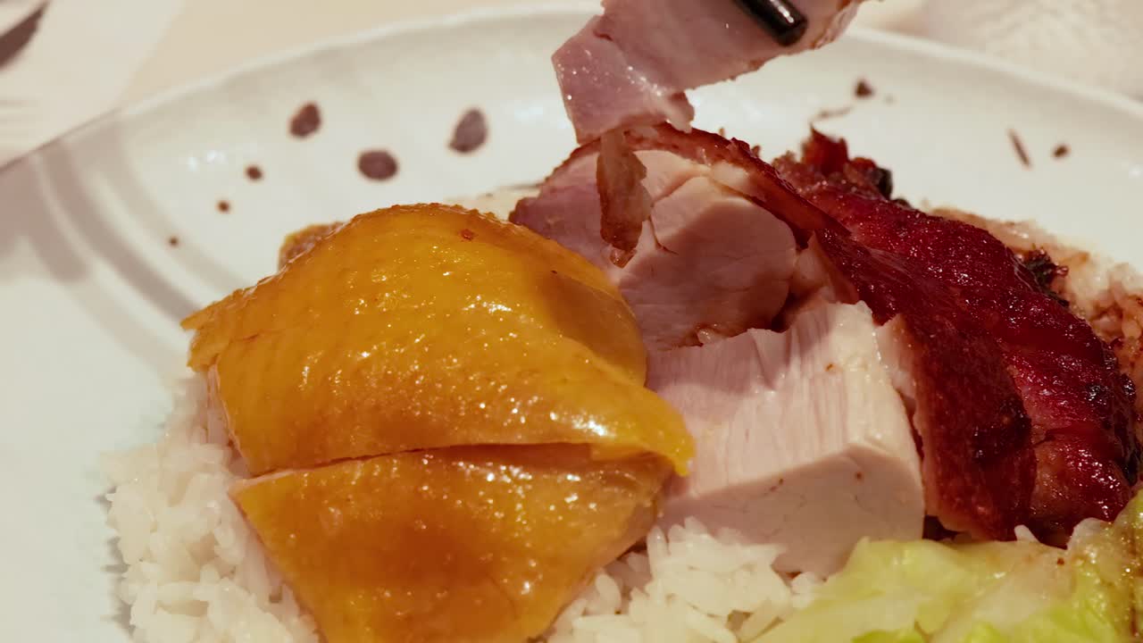 Close-up of chopsticks picking roast meats from a plate with rice and cabbage.