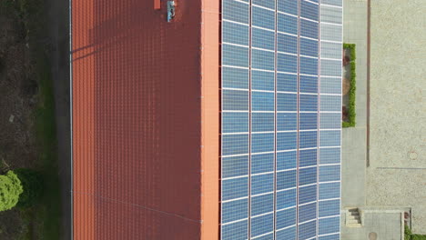 Una-Toma-Aérea-Desde-Arriba-Muestra-Una-Amplia-Gama-De-Paneles-Solares-Azules-Cuidadosamente-Dispuestos-En-El-Techo-De-Terracota-De-Un-Edificio,-Destacando-Las-Prácticas-De-Energía-Sostenible.