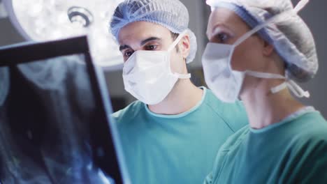 Video-of-caucasian-male-and-female-surgeon-studying-x-ray-in-operating-theatre