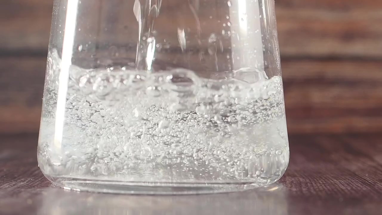 Liquido trasparente che si versa in un matraccio di vetro con bolle.