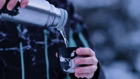 thermos pours tea into mug in the middle of cold winter landscape