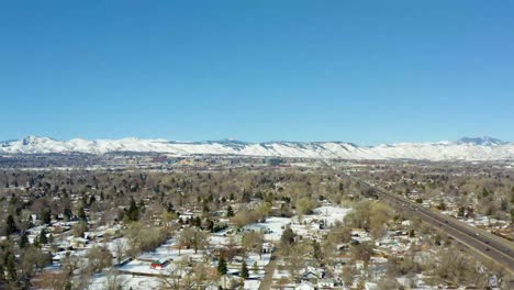 an aerial side moving shot of the roads in a city overlooking a snowy mountain in denver during the winter