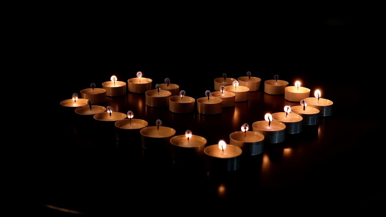 Lumi di tealight tremolanti a forma di cuore che mostrano pozze di cera su un tavolo scuro mentre la camera si avvicina, proiettando una luce