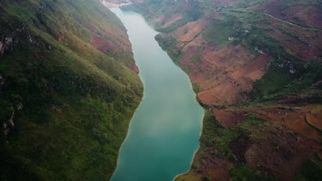 an aerial shot looking down at a turquoise reflective river reveals a dam in the distance