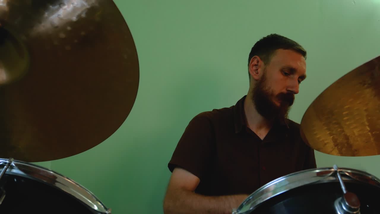 baterista calentándose con pinceles de batería. hombre barbudo tocando música rock y metal en la batería en el fondo de la pared verde. ensayo de la banda de música atascando imágenes de 4k.