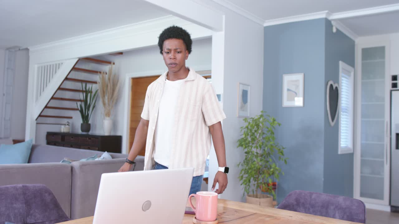 After stretching, man moving to laptop on wooden table at home, checking screen for work