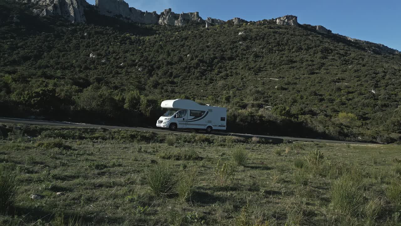White Caravan Car Drives Uphill Green Mountains of South France, RV Motorhome in European Summer Landscape, Aerial Drone View