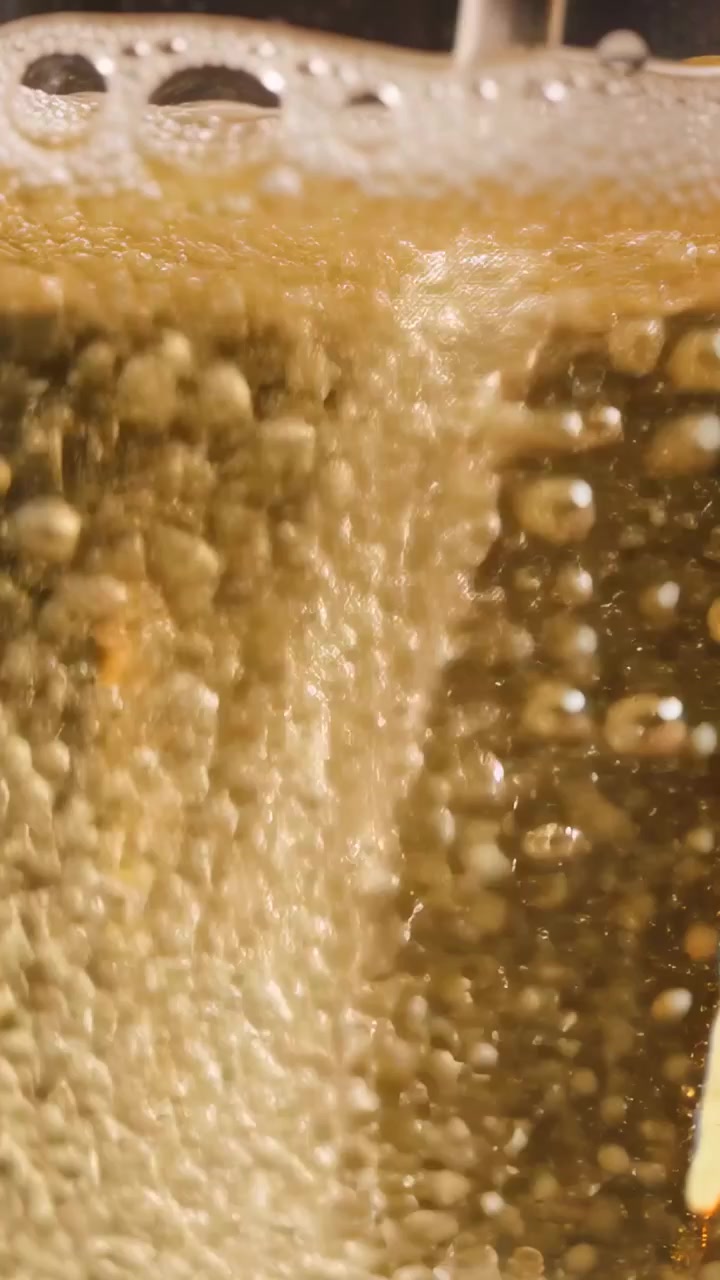 Video verticale: Beccuccio che versa bibita ambrata in un bicchiere trasparente su un bancone da bar, mentre si riempie e fa schiuma.