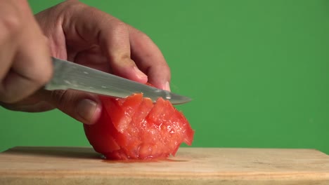 mani con un coltello tagliando a cubetti un pomodoro su uno sfondo cromatico