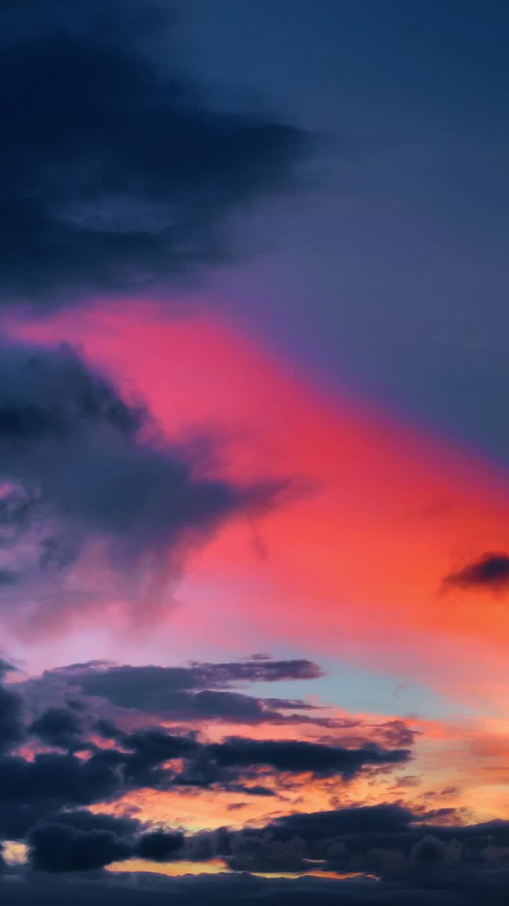 Vibrant sunset clouds with pink and orange colors. Abstract sky background featuring dark blue and purple clouds illuminated by bright pink and orange sunset light