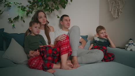 Kaukasische-Familie-Sitzt-Während-Der-Weihnachtsferien-Zusammen-Auf-Einem-Sofa-Und-Schaut-Zu-Hause-Fern-Und-Dekoriert-Die-Wohnungseinrichtung.-Hochwertiges-4K-Filmmaterial