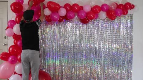 man decorating valentines day balloons and iridescent fringe curtain