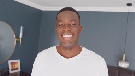 Video-portrait-of-happy-african-american-man-smiling-to-camera-in-bedroom-at-home
