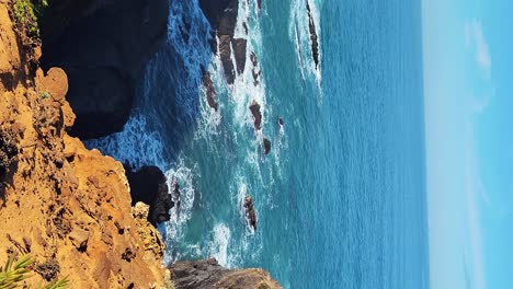 Zambujeira-do-Mar-over-the-sea-shore-with-ocean-waves,-cliffs-and-sand-dunes-covered-by-green-vegetation-red-leaves-of-sour-fig,-sunny-day,-clear-blue-sky