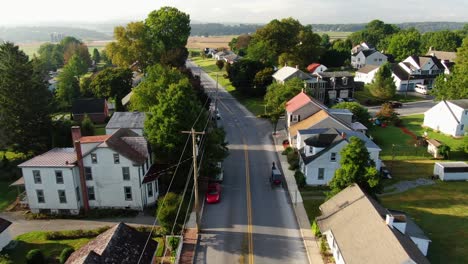 Aerial-drone-dolly-forward-following-Amish-horse-and-buggy-out-of-town-into-rural-farmland-in-Lancaster-County,-Pennsylvania