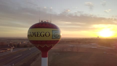 wamego water tower with bright white sun in background at sunset, kansas, aerial pan