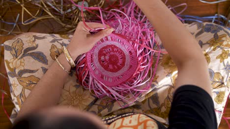 overhead view of an indigenous woman hand weaving a colorful basket