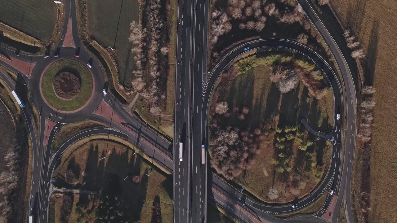 Overhead drone video capturing the highway with roundabouts, while moving cars and trucks.