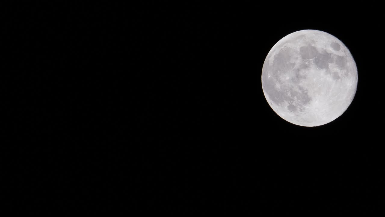 Time lapse of a full moon in a dark sky The surface of the moon shows some craters and texture