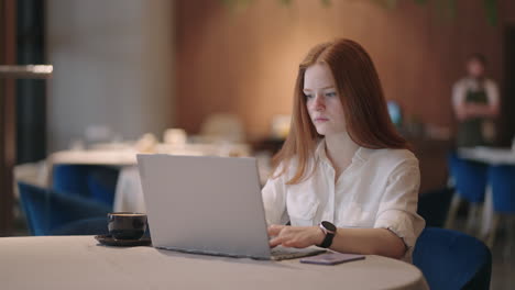 Pretty-student-woman-using-laptop-in-outdoors-cafe-while-having-cup-of-coffee.-Cheerful-woman-working-at-cafe-on-laptop.-Businesswoman-working-during-layover-at-modern-airport.