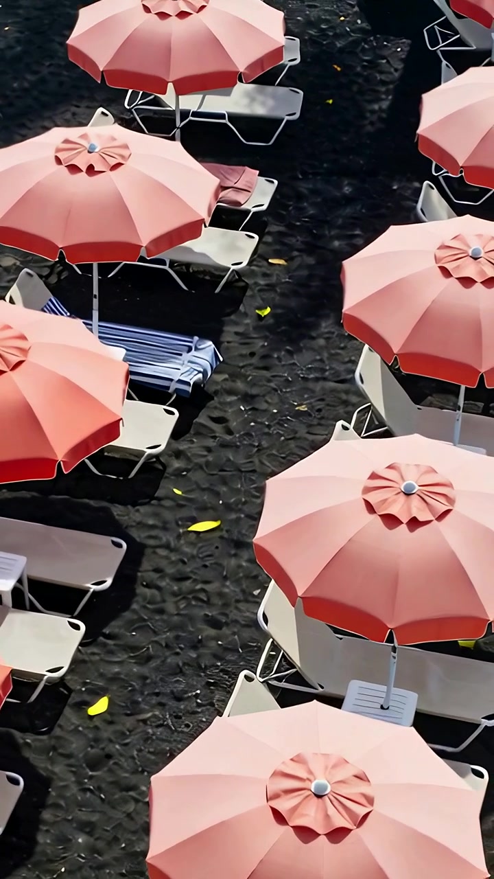 Video verticale: Ripresa dall'alto che scende mostrando ombrelloni e sedie rosa corallo in spiaggia con asciugamani.