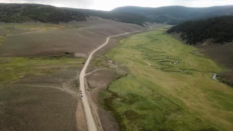 High-aerial-view-following-an-alpine-meadow-with-a-crooked-creek-in-the-Colorado-Rocky-Mountains-on-a-cloudy-day