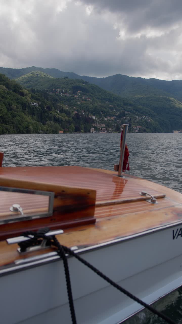 Vertical shot of the back of a speedboat floating at the dock with a small town in the background at Lake Como, Italy (Lago di Como, Italia), peaceful and scenic