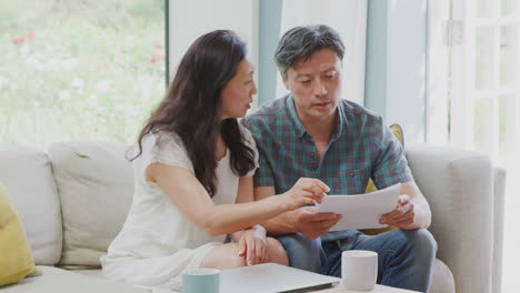 Mature-Couple-Sitting-On-Sofa-At-Home-Reviewing-Personal-Finances-On-Laptop