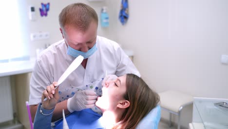 doctor working with patient in dental clinic. male stomatologist treating patien's teeth in dentist room. girl holding mirror while specialist checking teeth. stomatology concept.