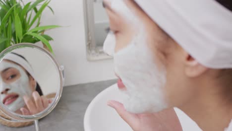 biracial woman applying cream on face in bathroom